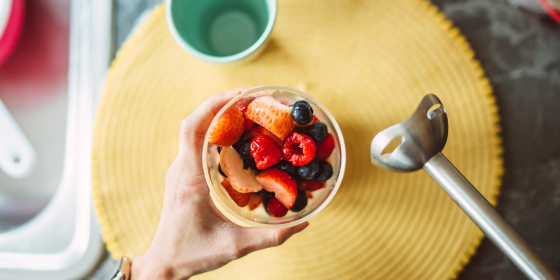 Overhead view of a cup of fruit and an immersion blender