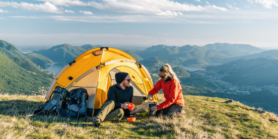 Couple sitting in front of a yellow camping tent, overlooking the mountains