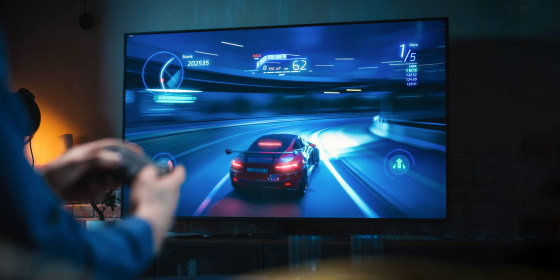 Close Up on Man's Hands at Home, Sitting on a Couch in Stylish Loft Apartment and Playing Arcade Car Video Games on Console. Male Using Controller to Play Street Racing Drift Simulator.