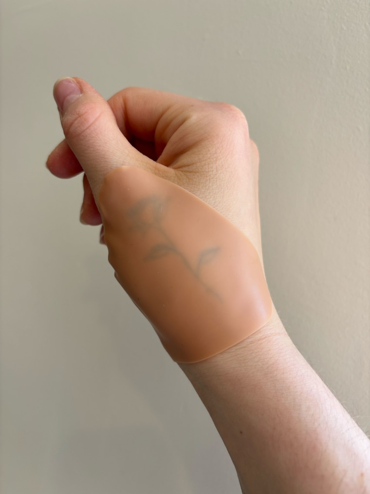 A Sun Patch Hand and Cheek Patch covering a hand tattoo of a rose against a beige background.