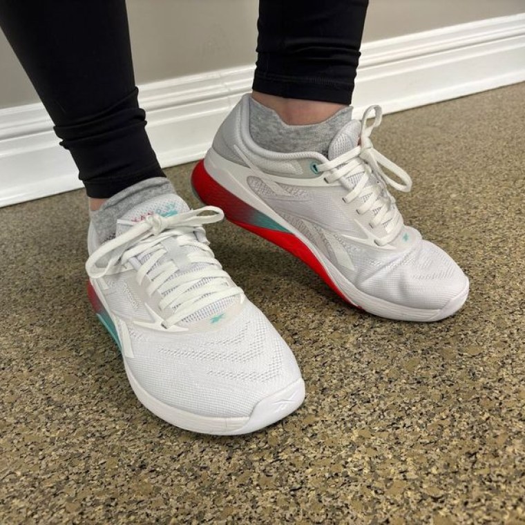 A woman wearing a pair of white Reebok Nano X5 training shoes at the gym.