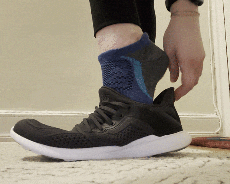 A GIF of a person slipping their foot into a black APL TechLoom Tracer training sneaker.