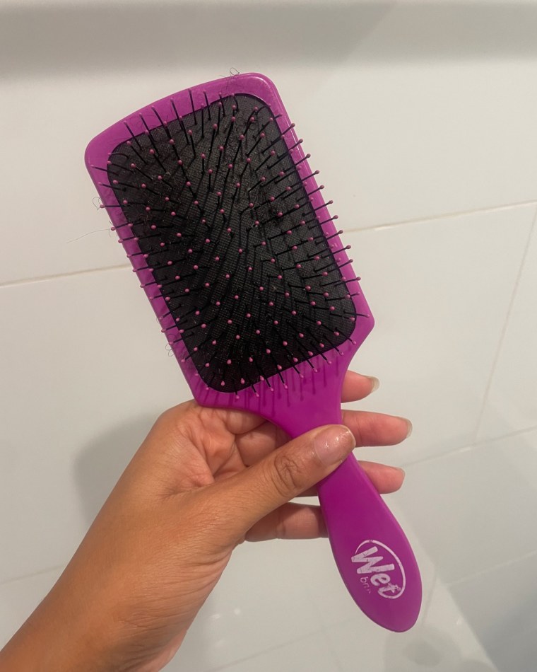 Woman holding purple hairbrush against white wall