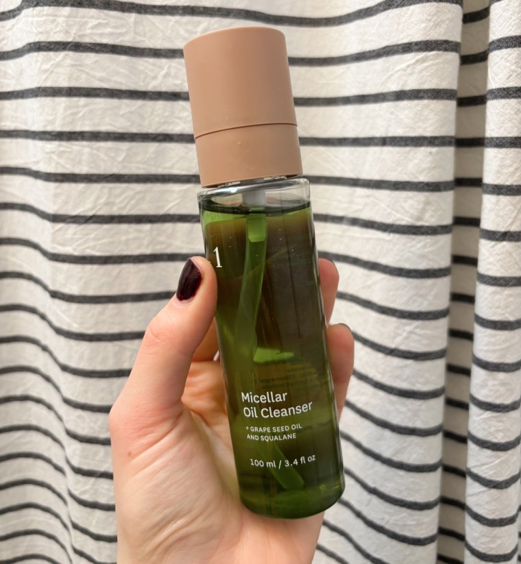 Woman holding bottle of Fig 1 cleanser against striped curtain background
