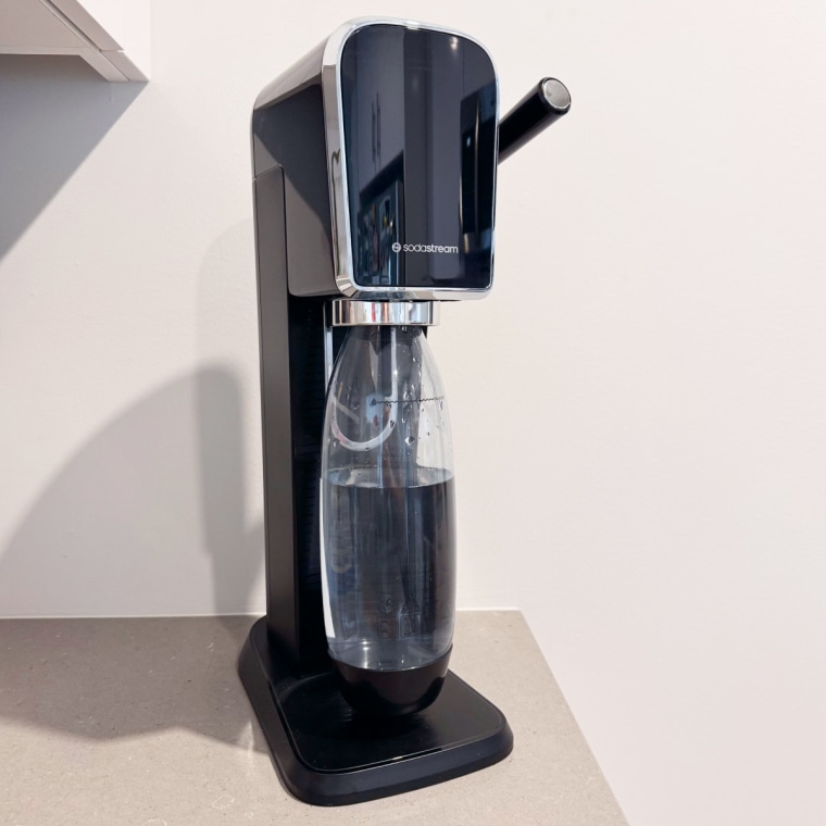 Sodastream Art sitting on a countertop beside a cabinet.