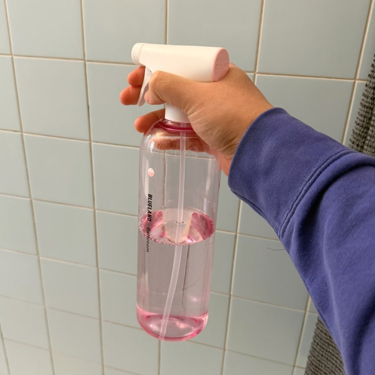 Person holding Blueland bathroom spray in front of tile wall.