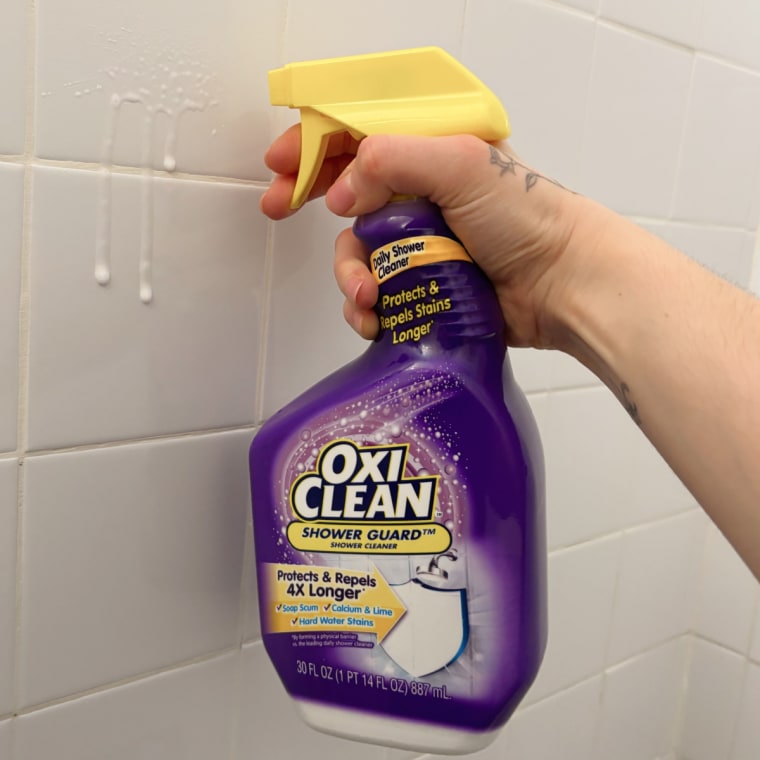 Person holding bottle of Oxiclean Shower Guard spray in front of a tile wall.