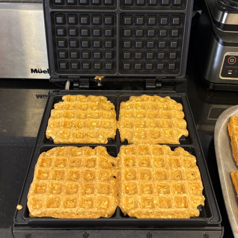 A Krups 4-Slice Belgian Waffle Maker with golden brown waffles inside it on a black countertop.