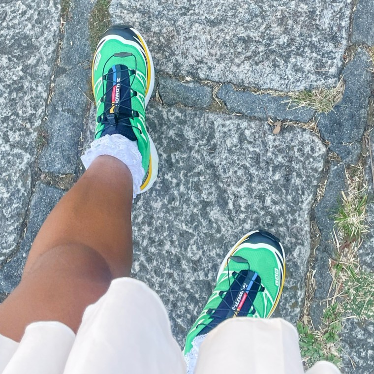 The green and yellow Salomon XT-6 sneakers on stone-paved ground.