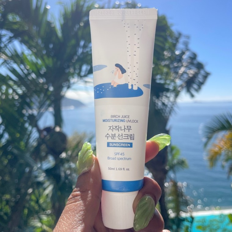 The Round Lab Birch Moisturizing Sunscreen in front of a tropical daytime background of palm trees, the ocean and a pool.