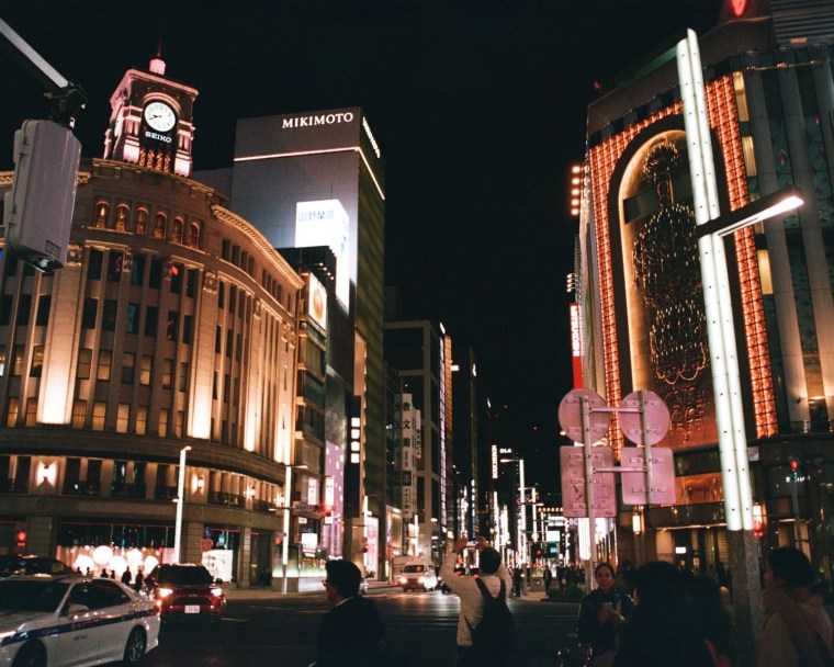 A photo of a busy street at night, flanked by tall, illuminated buildings.