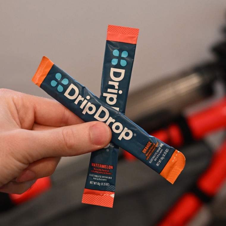 A close up of a man holding two packets of DripDrop drink mix.