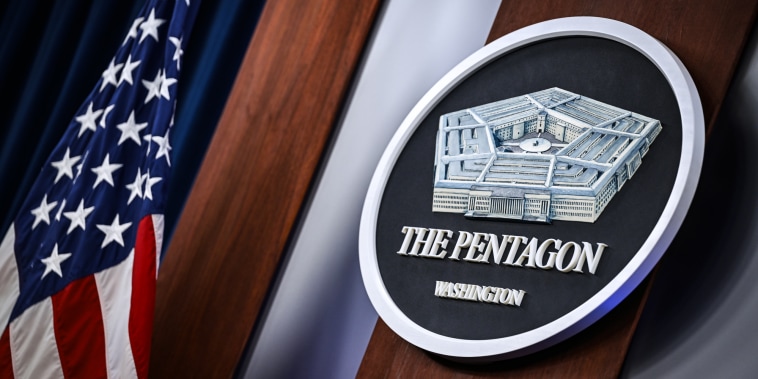 The Pentagon crest logo is on a wall next to an American flag